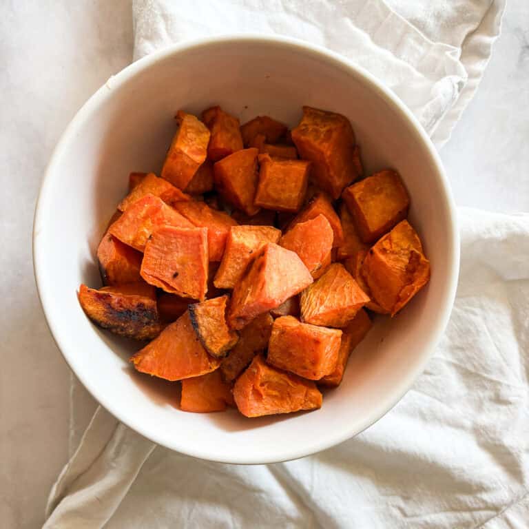 A bowl of baked sweet potato cubes placed on top of a white napkin.