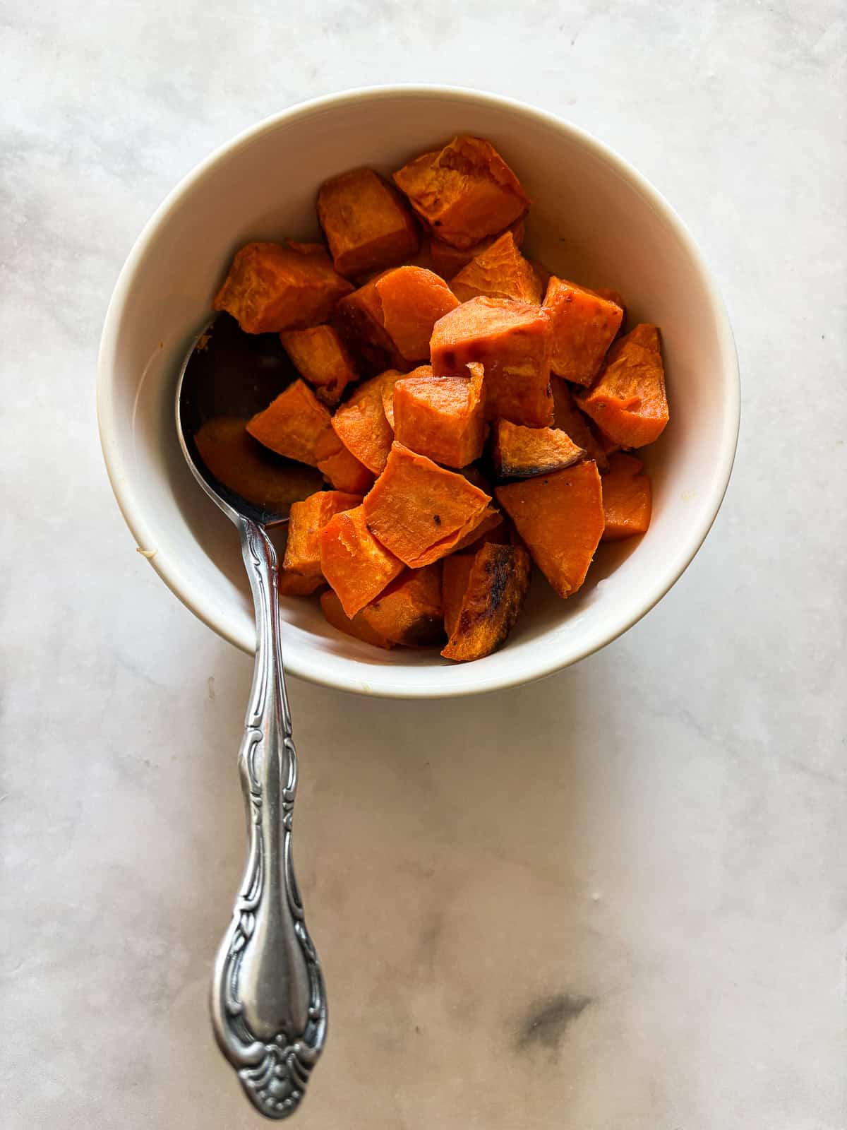 Cubed sweet potatoes are dressed in olive oil and salt and baked until sweet and soft. A great weeknight or holiday side dish. A serving spoon rests in a bowl of baked sweet potatoes.