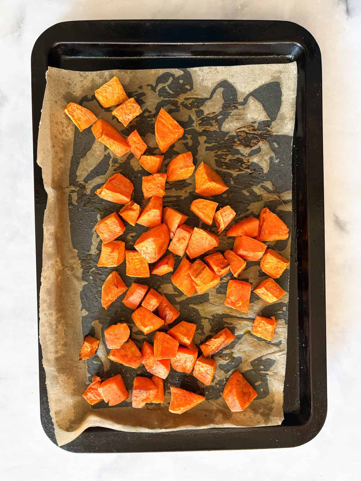 Cubed sweet potatoes are dressed in olive oil and salt and baked until sweet and soft. A great weeknight or holiday side dish. Baked sweet potato cubes after coming out of the oven.