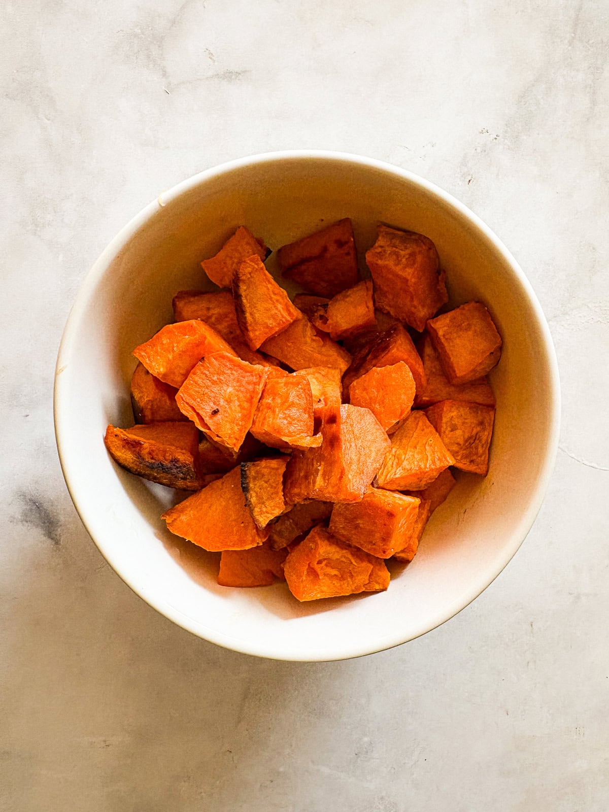 Cubed sweet potatoes are dressed in olive oil and salt and baked until sweet and soft. A great weeknight or holiday side dish. A bowl of baked sweet potato cubes.