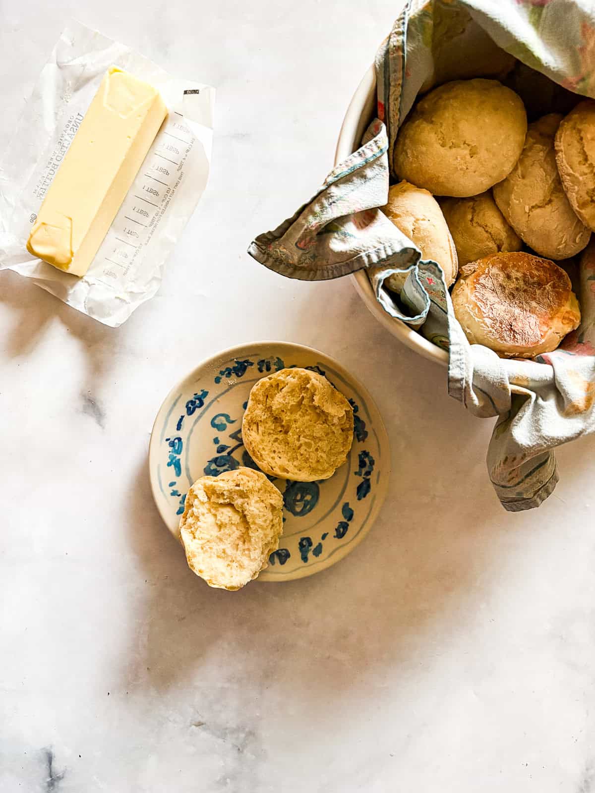 Tender and light soda biscuits need just five simple ingredients and an easy prep method - a keeper of a recipe! A stick of butter, a soda biscuit cut in half on a plate, and a bowl of biscuits.