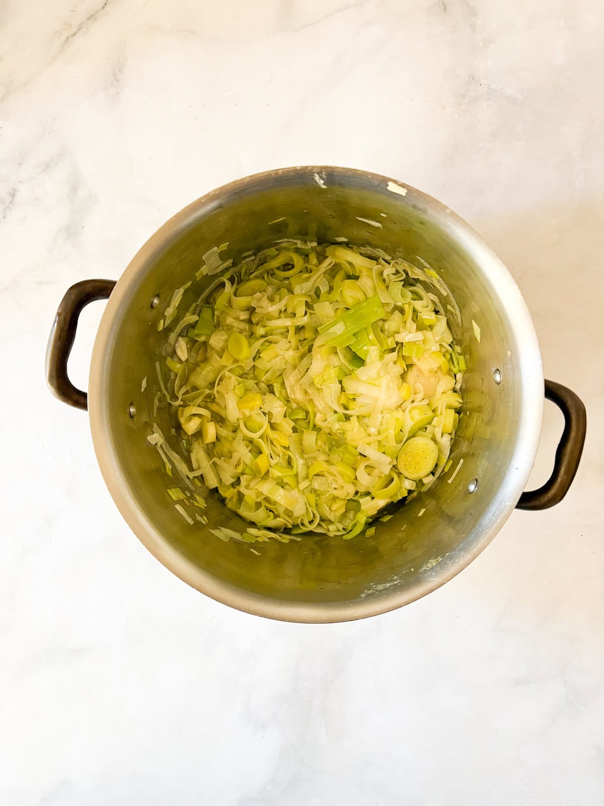 Rich and smooth vegetarian potato leek soup is made from simple ingredients that transform into something deliciously memorable. Leeks are cooked down in a pot for vegetarian potato leek soup.