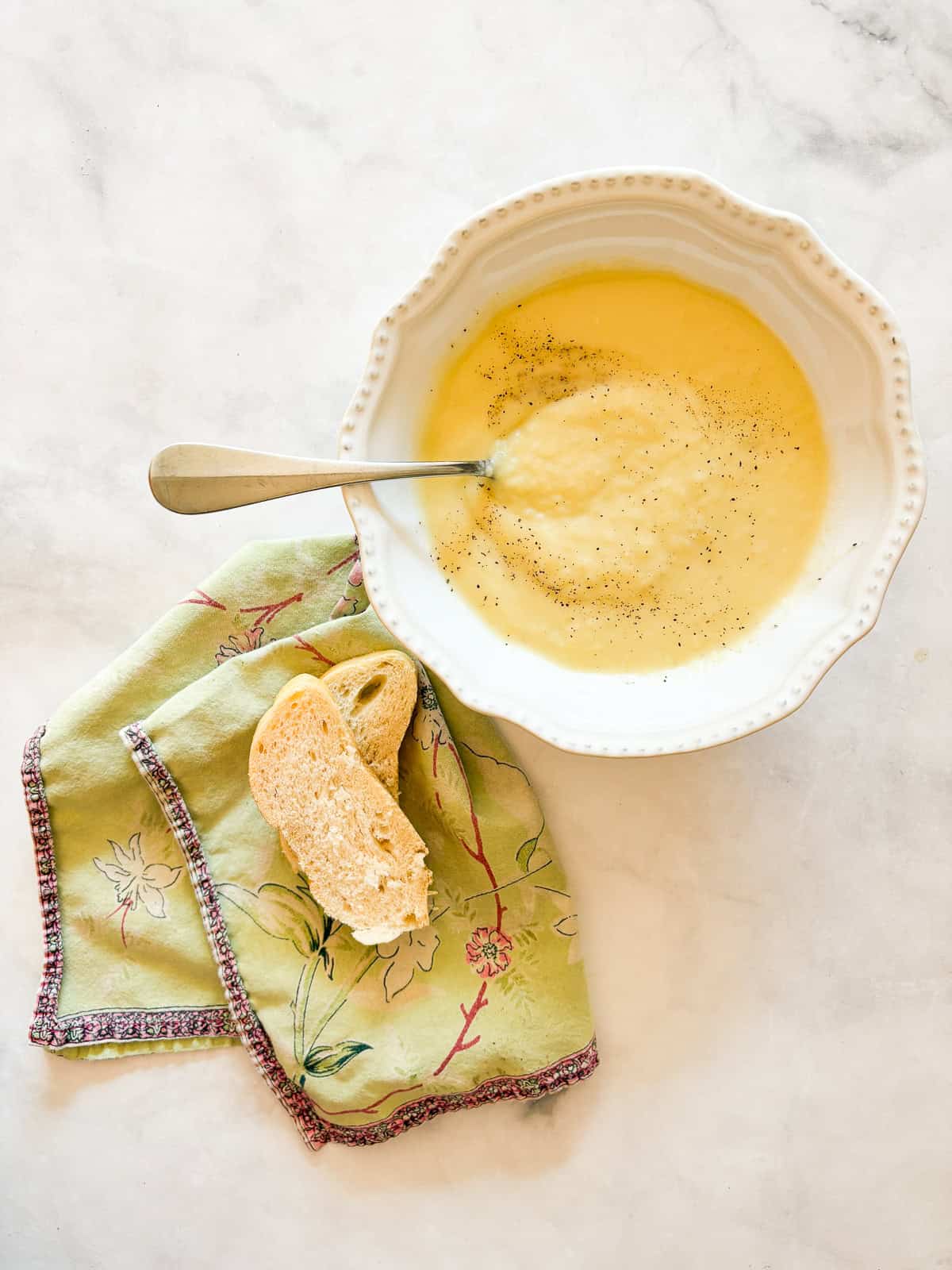Rich and smooth vegetarian potato leek soup is made from simple ingredients that transform into something deliciously memorable. A bowl of vegetarian potato leek soup with a spoon in it next to a napkin with slices of bread.
