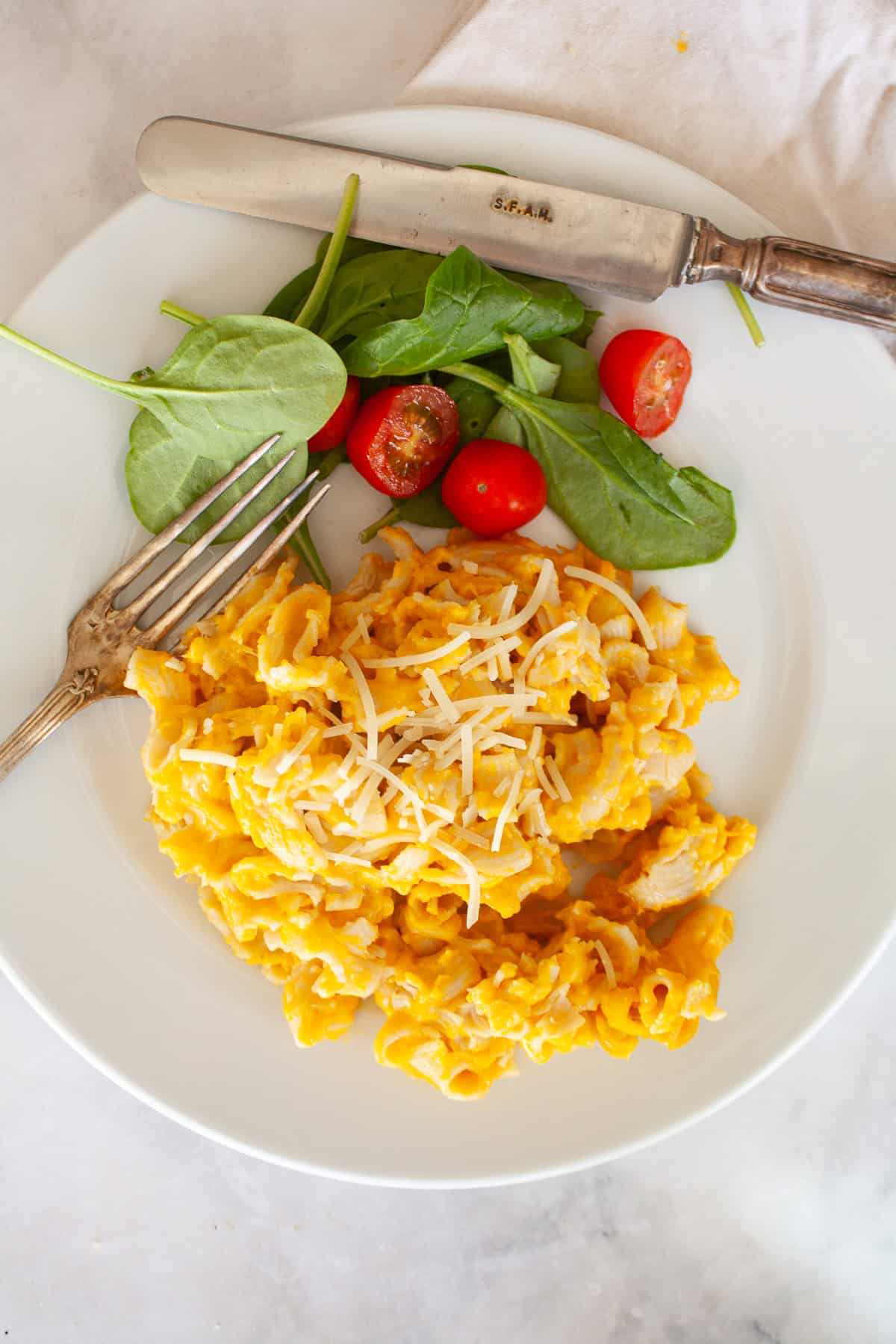 A fork rests on a plate with a serving of butternut squash mac and cheese and salad.