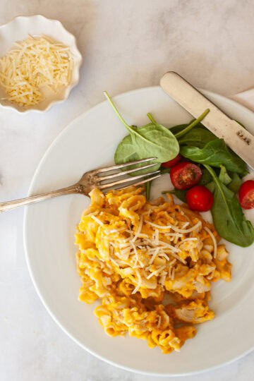 A plate of butternut squash mac and cheese and salad with a fork and cheese.