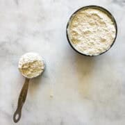 A bowl of homemade gluten free bread flour and a measuring cup with flour.