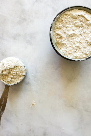 A bowl of homemade gluten free bread flour and a measuring cup with flour.