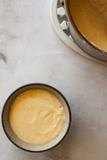 A pot of gluten free cheese sauce with a wooden spoon next to a bowl of sauce.