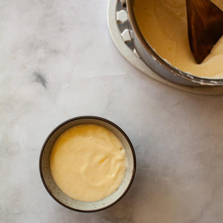 A pot of gluten free cheese sauce with a wooden spoon next to a bowl of sauce.