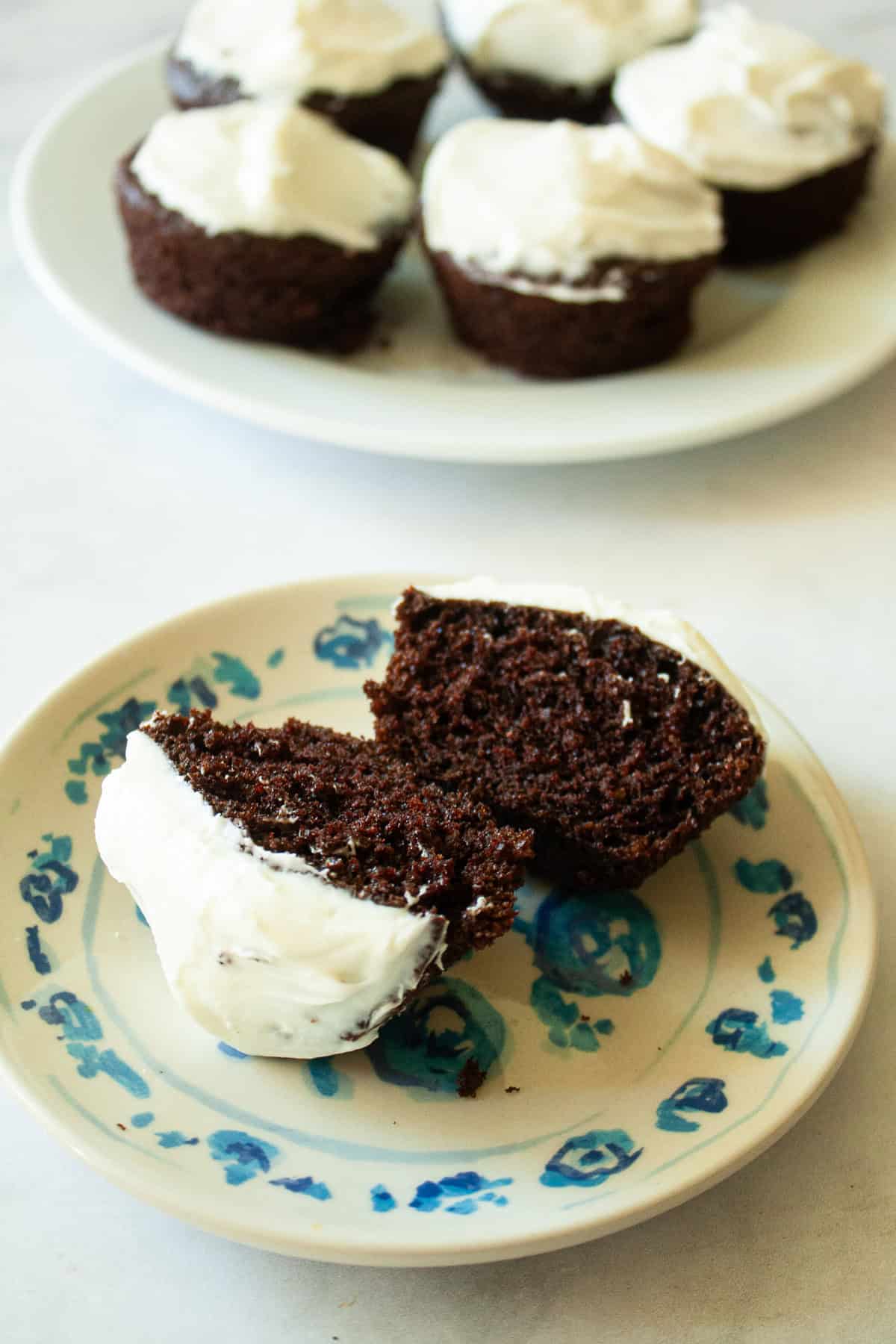 Gluten free Guinness chocolate cupcakes are dark, rich, and topped with a tangy-sweet cream cheese frosting. A Guinness chocolate cupcake cut in half on a plate with more cupcakes nearby.