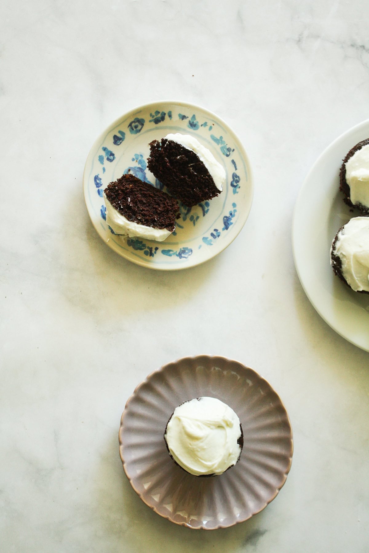 Gluten free Guinness chocolate cupcakes are dark, rich, and topped with a tangy-sweet cream cheese frosting. Guinness chocolate cupcakes, one on a plate, and one cut in half.
