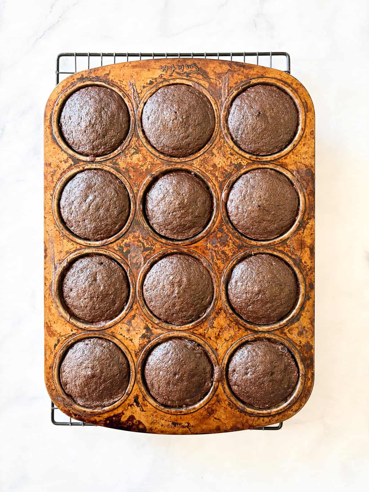 Gluten free Guinness chocolate cupcakes are dark, rich, and topped with a tangy-sweet cream cheese frosting. Gluten free Guinness chocolate cupcakes cool in a cupcake tin.