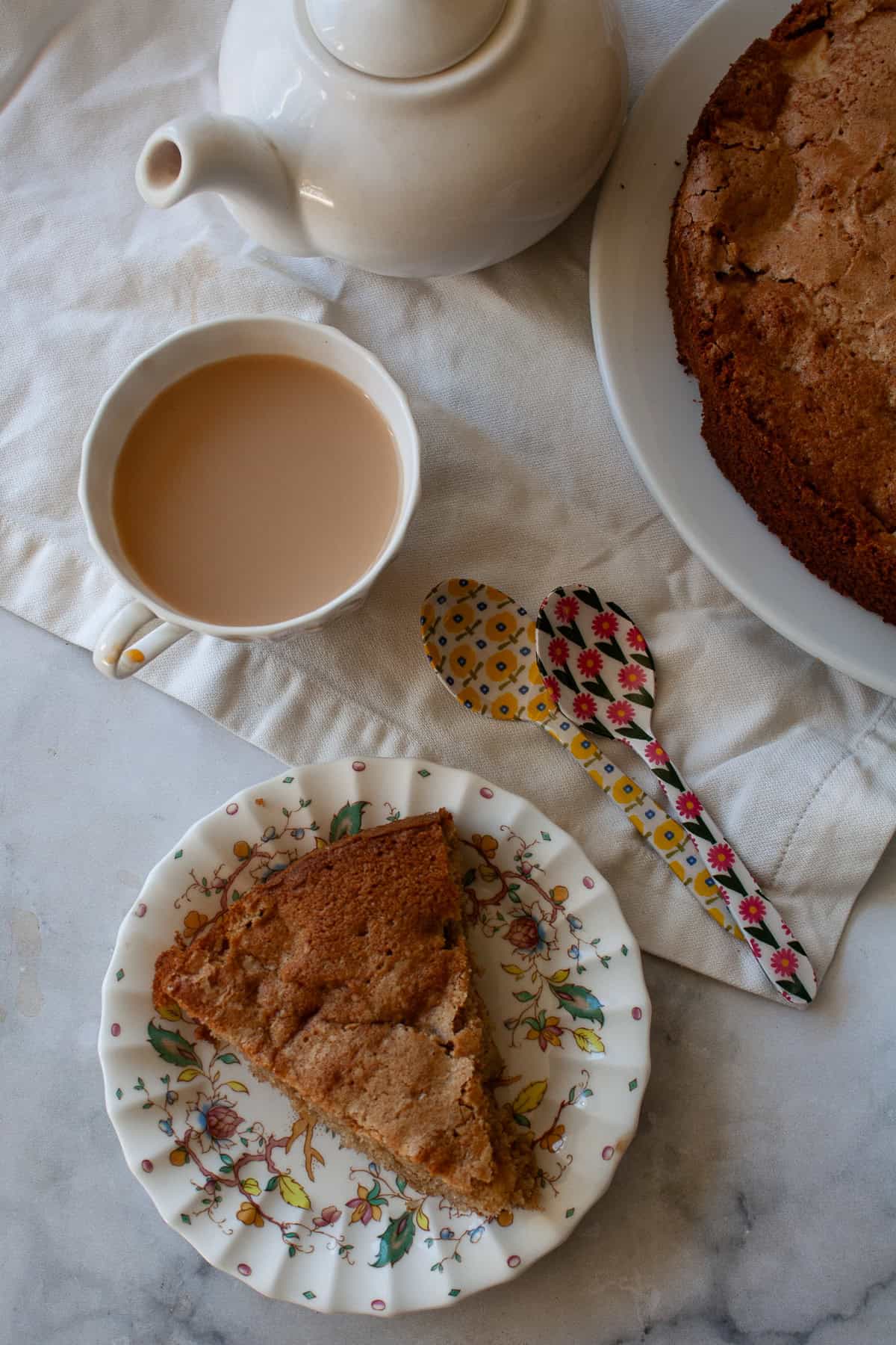 A soft and sweet gluten free Irish apple cake that's inspired by a traditional Irish recipe. Delicious plain, it can be served warm or cold. A slice of gluten free Irish apple cake on a plate and a cup of tea.