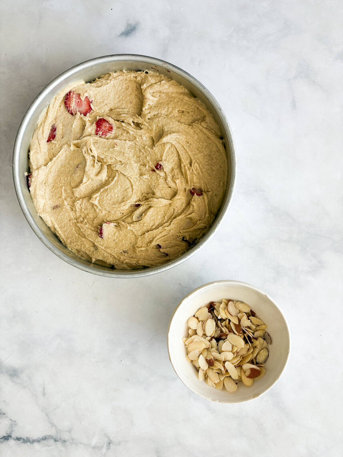 A gorgeous gluten free strawberry almond cake loaded with fresh fruit and topped with toasted almonds and a shower of powdered sugar. Strawberry almond cake batter added to a cake pan.