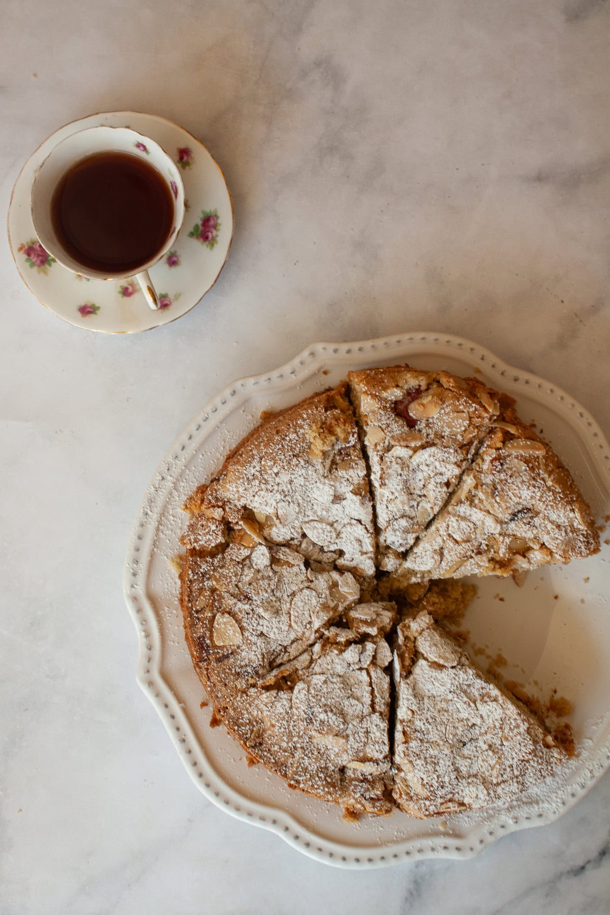 A gorgeous gluten free strawberry almond cake loaded with fresh fruit and topped with toasted almonds and a shower of powdered sugar. A gluten free strawberry almond cake and a cup of tea.