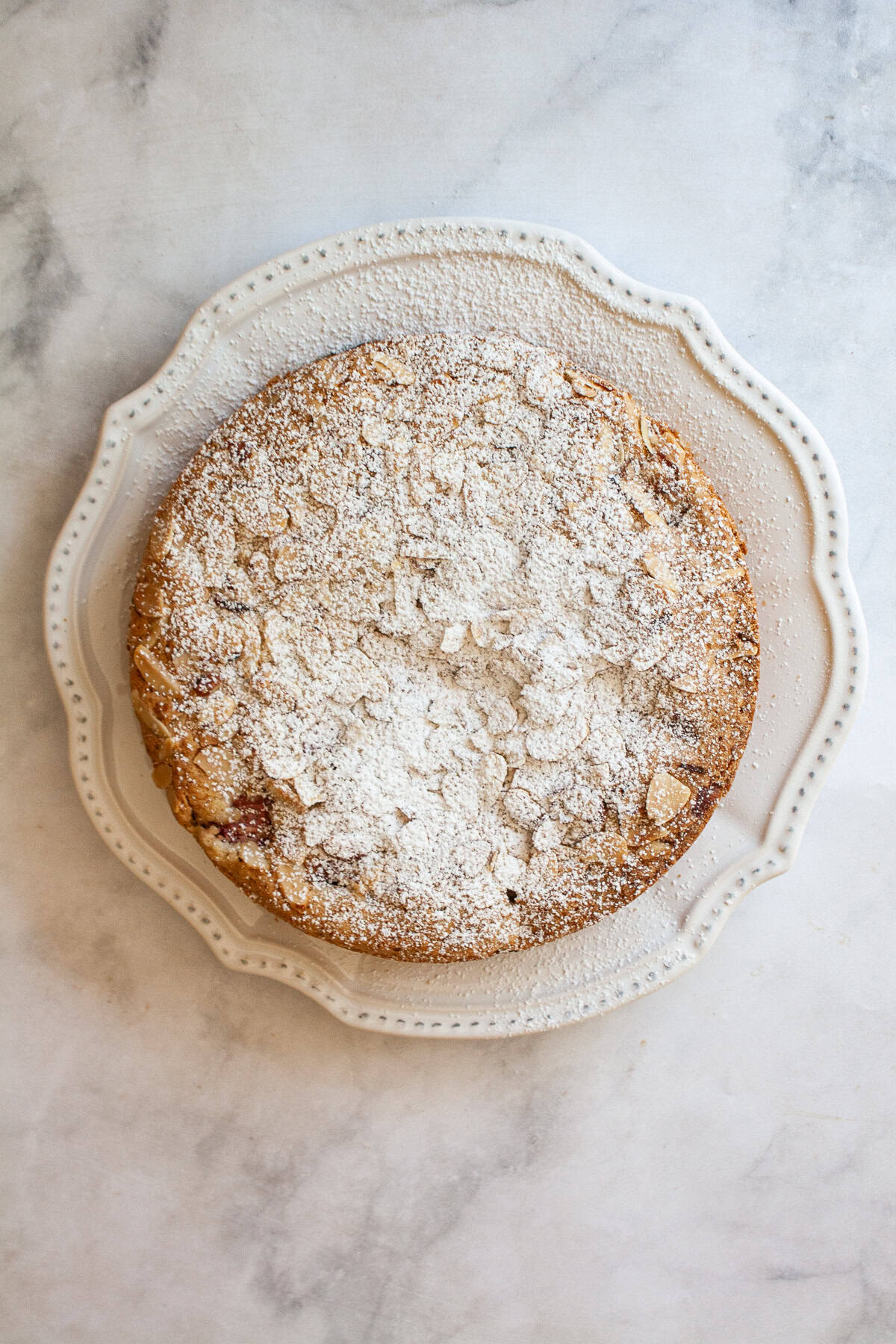 A gorgeous gluten free strawberry almond cake loaded with fresh fruit and topped with toasted almonds and a shower of powdered sugar. A gluten free strawberry almond cake on a white plate.