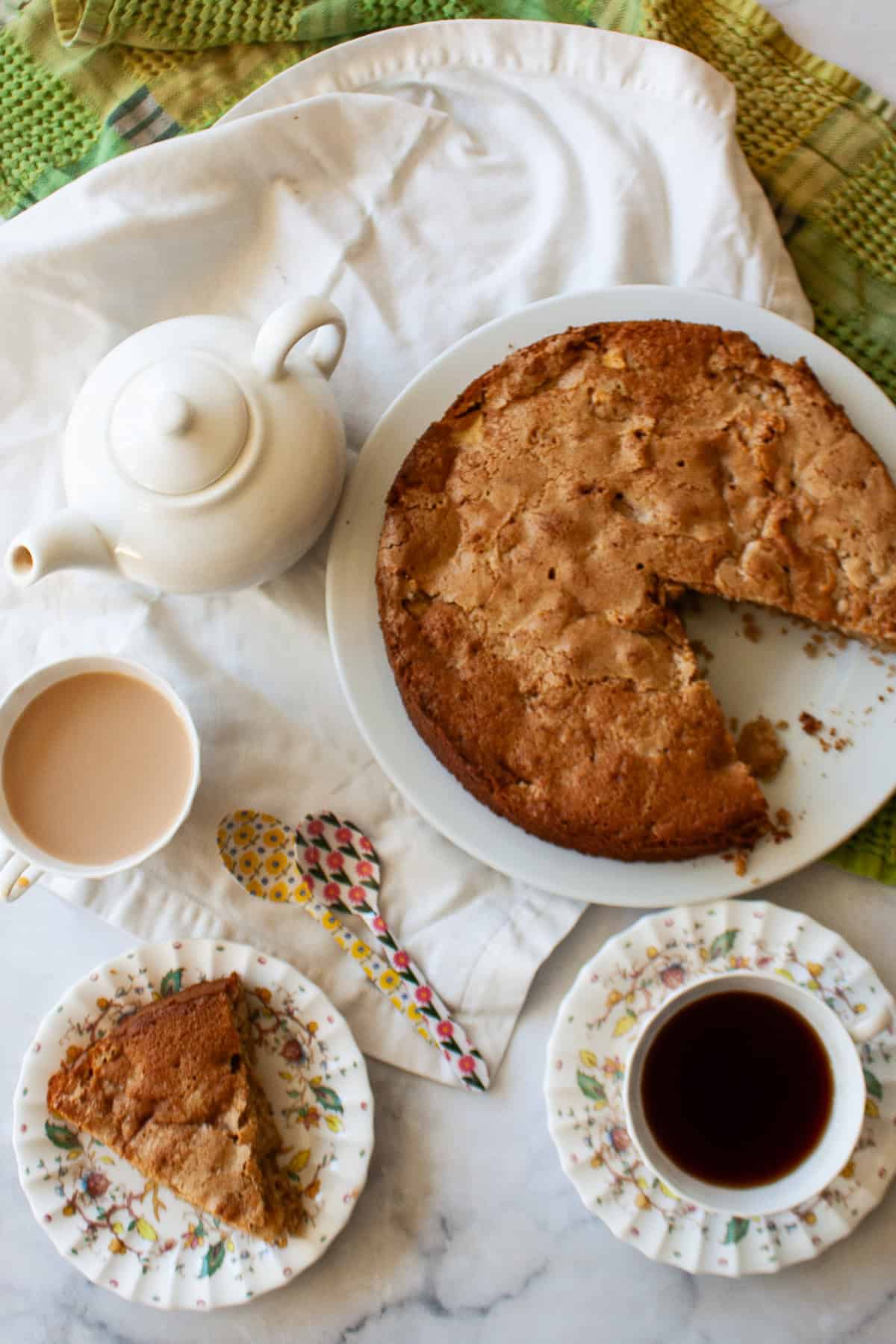 A soft and sweet gluten free Irish apple cake that's inspired by a traditional Irish recipe. Delicious plain, it can be served warm or cold. A white tea pot and cups of tea next to a gluten free Irish apple cake.