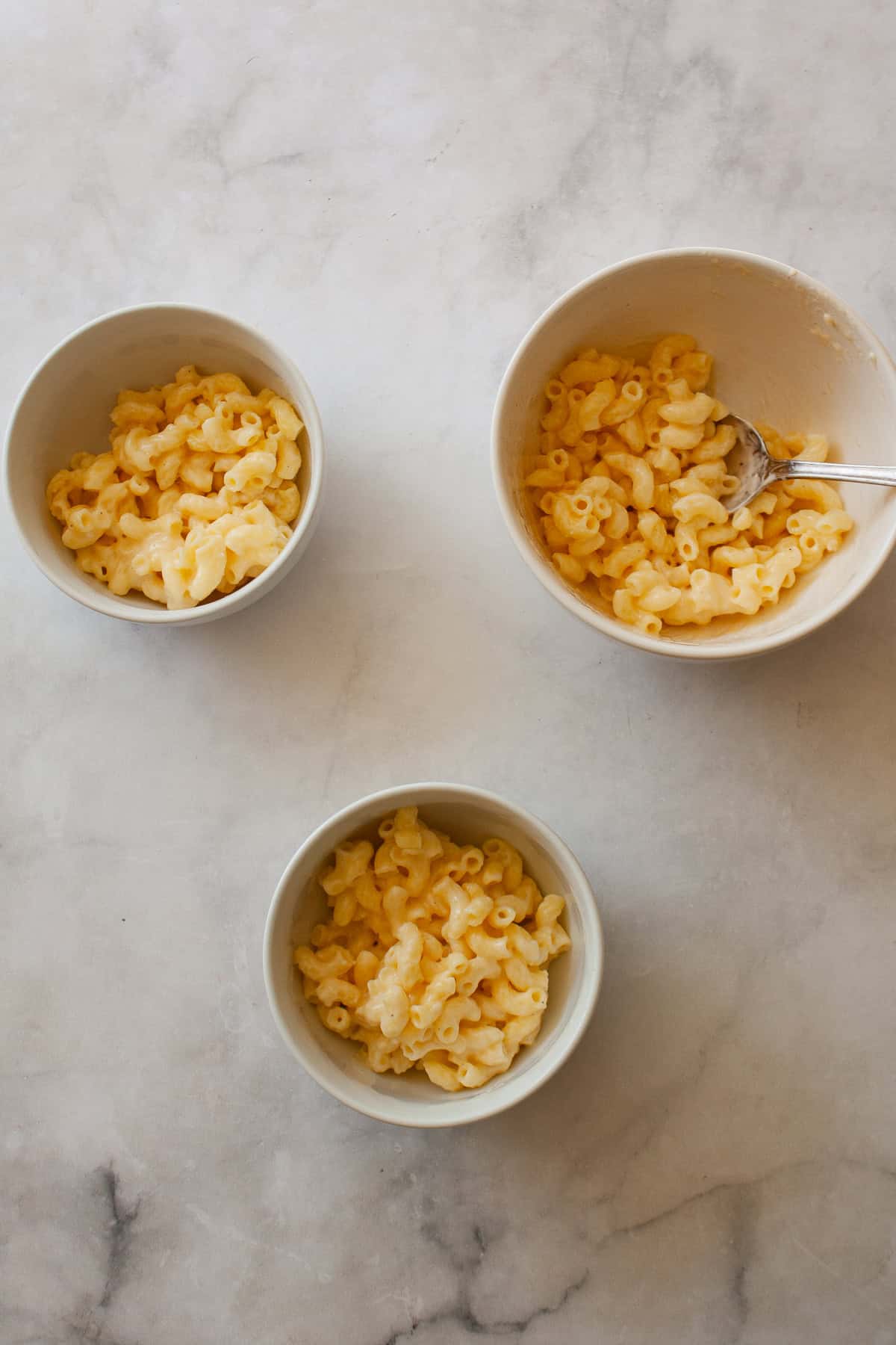 Every bite of this creamy, one pot gluten free mac and cheese delivers homemade comfort - so much better than store-bought! Fast and easy. A serving bowl of one pot gluten free mac and cheese and two servings in smaller bowls.
