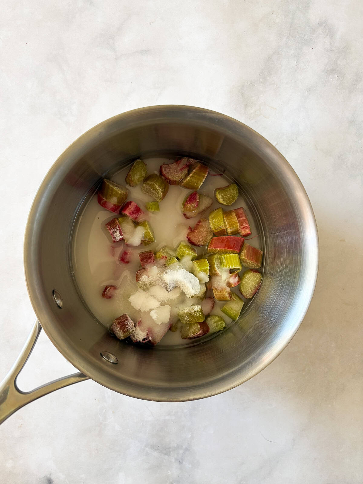 Gorgeously hued and perfectly sweet-tart, rhubarb simple syrup is a delightful addition to all sorts of drinks (and more). Rhubarb pieces, water, and sugar in a pot.