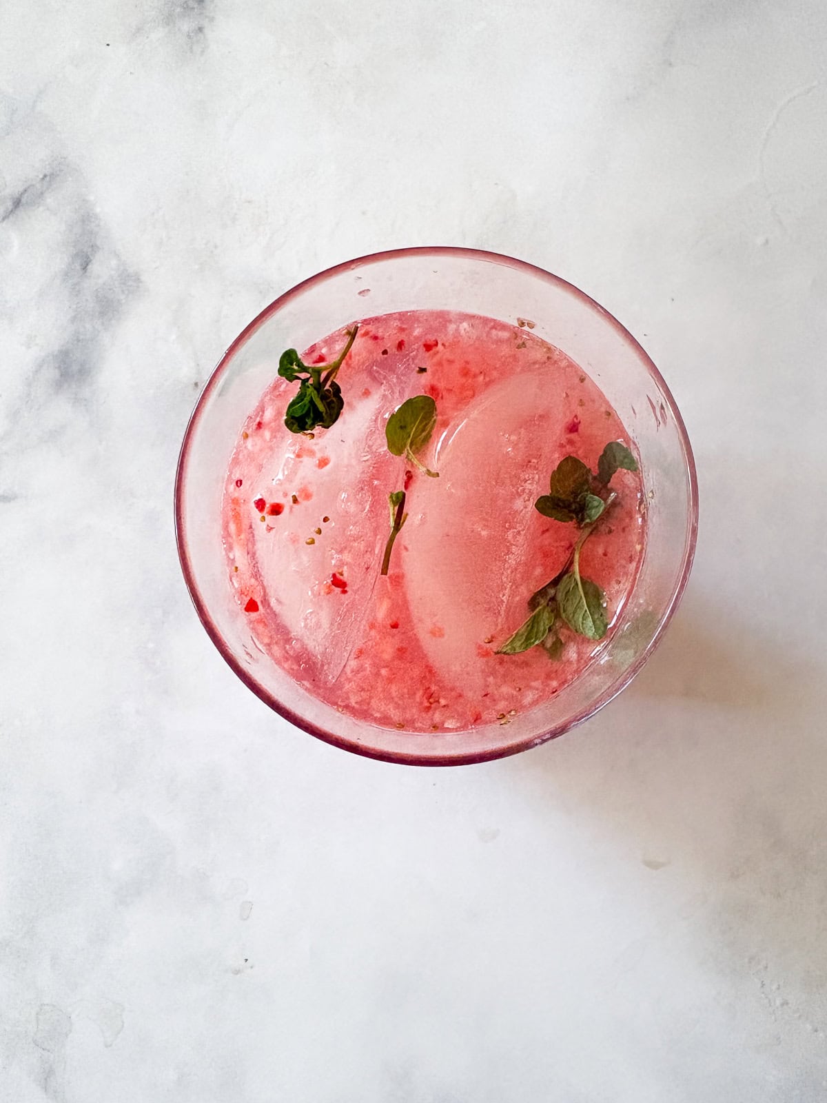 This beautiful strawberry cocktail can be made with or without gin, and is packed with fresh strawberries and mint! Mint floats in a glass of strawberry cocktail.
