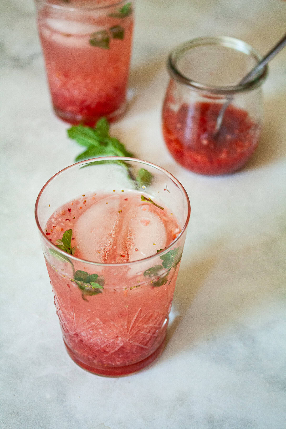 This beautiful strawberry cocktail can be made with or without gin, and is packed with fresh strawberries and mint! A glass of strawberry cocktail next to a jar of strawberry puree.