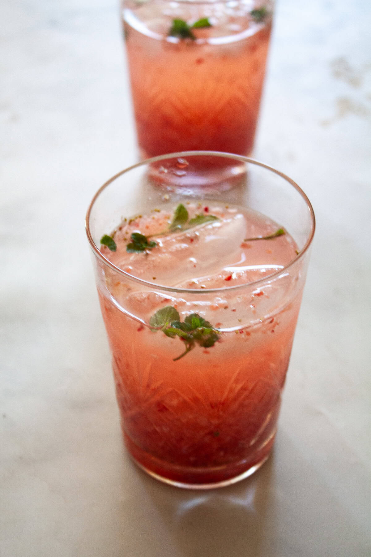 This beautiful strawberry cocktail can be made with or without gin, and is packed with fresh strawberries and mint! Two glasses of strawberry cocktail with ice.
