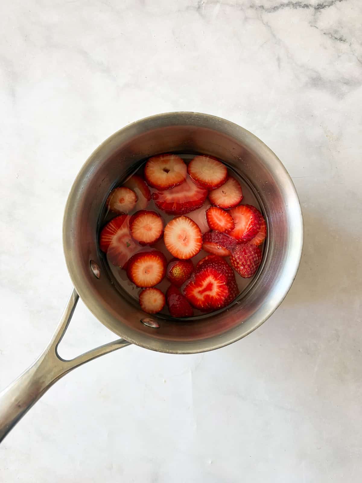 Three-ingredient strawberry simple syrup is so pretty when stirred into drinks or draped over cakes! A summer must-make. Strawberries, sugar, and water in a pot for strawberry simple syrup.