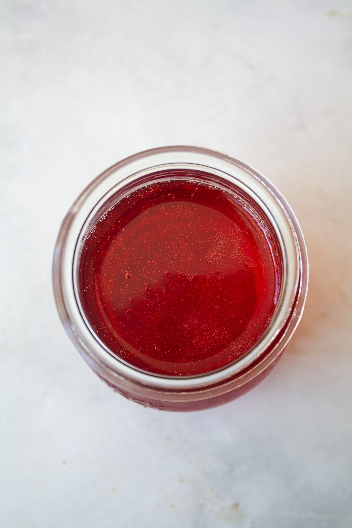 Three-ingredient strawberry simple syrup is so pretty when stirred into drinks or draped over cakes! A summer must-make. Strawberry simple syrup in a glass jar.