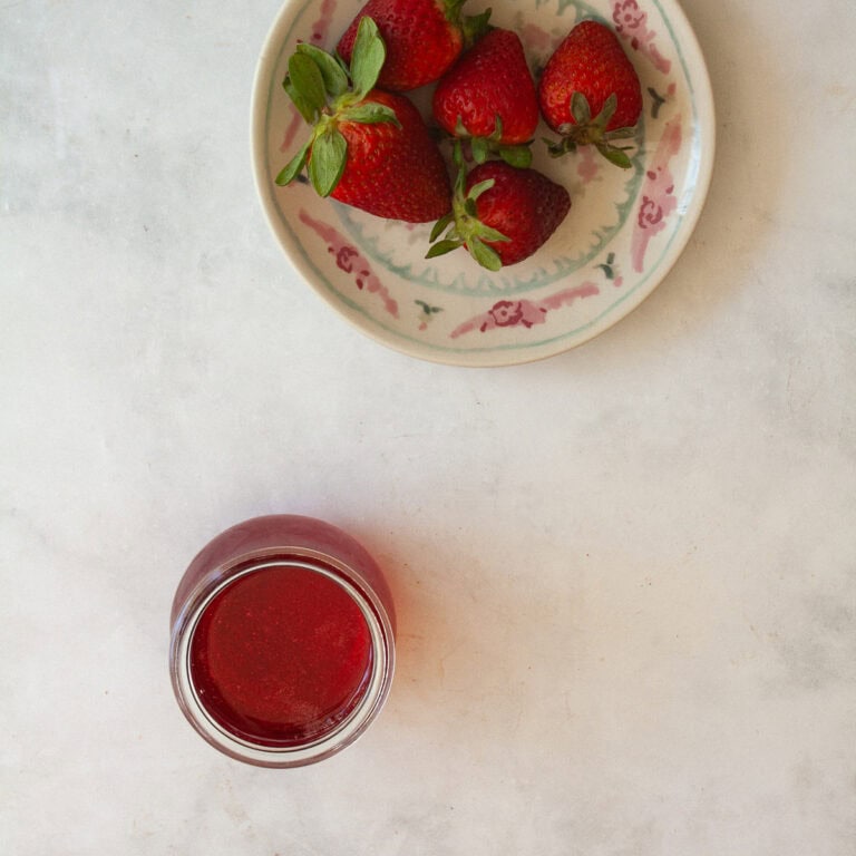 A jar of strawberry simple syrup and a plate of strawberries.