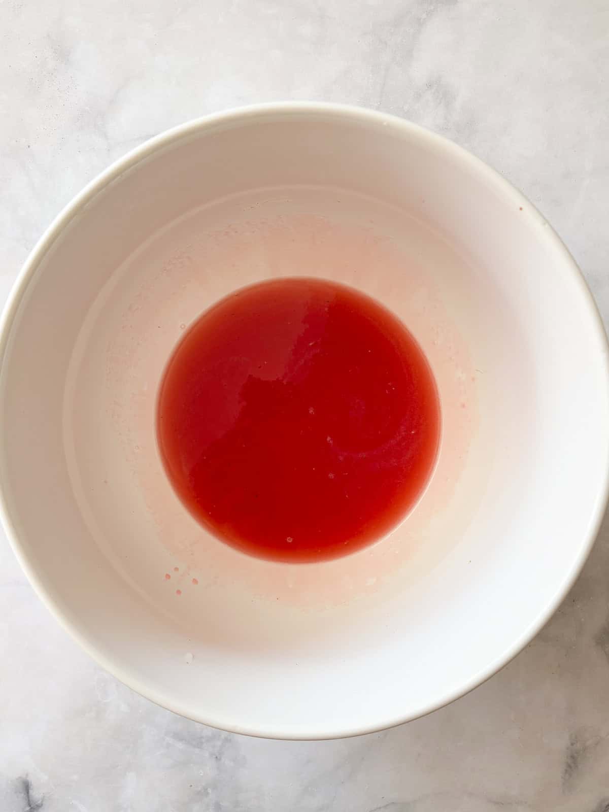 Three-ingredient strawberry simple syrup is so pretty when stirred into drinks or draped over cakes! A summer must-make. Strawberry simple syrup in a bowl.