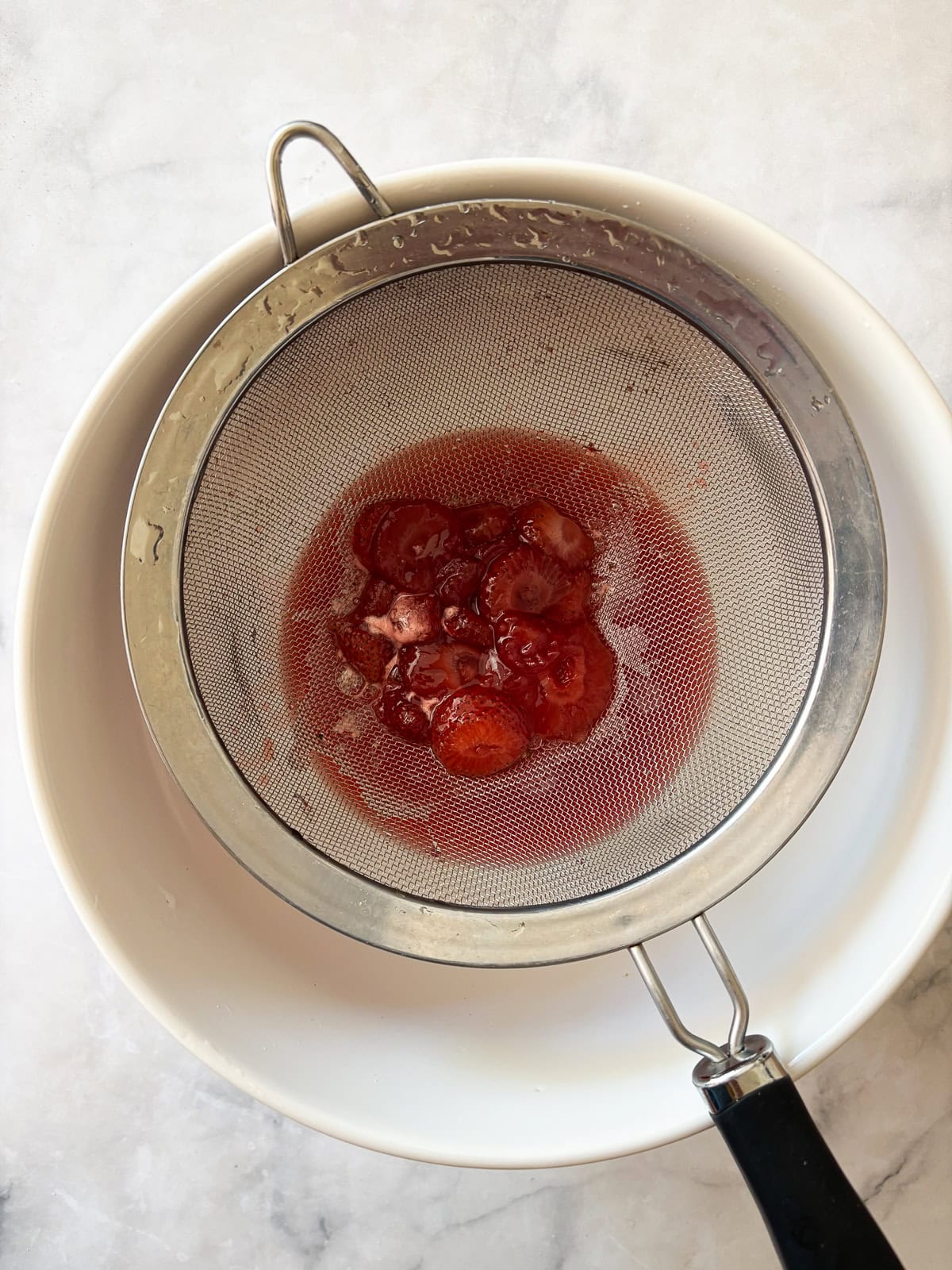 Three-ingredient strawberry simple syrup is so pretty when stirred into drinks or draped over cakes! A summer must-make. Straining strawberries out for strawberry simple syrup.