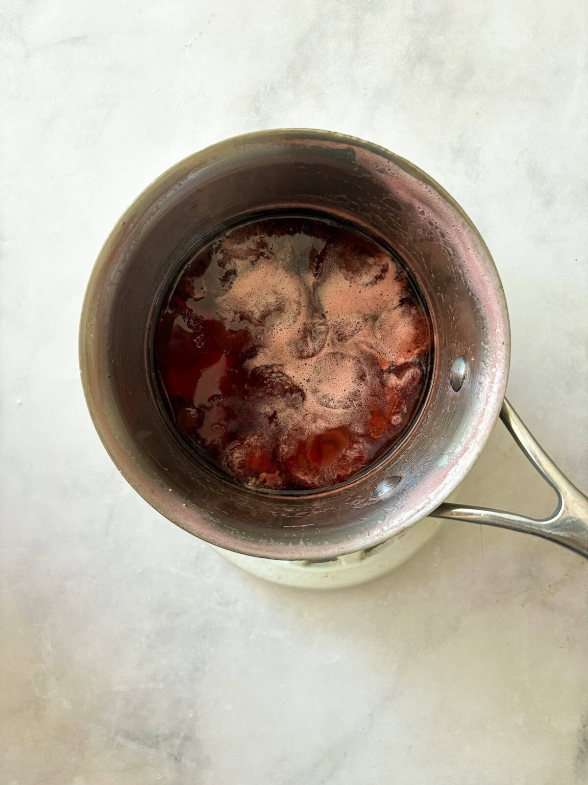 Three-ingredient strawberry simple syrup is so pretty when stirred into drinks or draped over cakes! A summer must-make. Strawberries cook down in a pot for strawberry simple syrup.