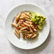 A plate of tomatoes and feta pasta with a cucumber salad alongside it.