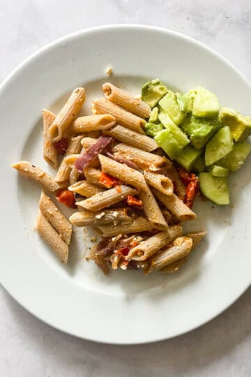 A plate of tomatoes and feta pasta with a cucumber salad alongside it.