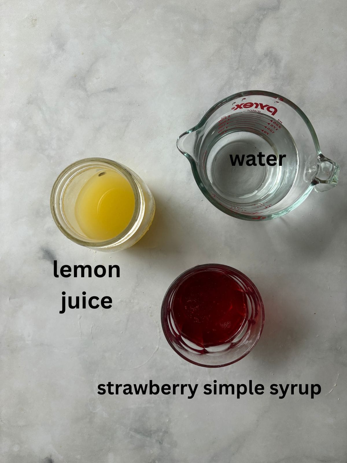 Sweet strawberry simple syrup is stirred into fresh lemon juice for a sweet-tart pitcher of homemade strawberry lemonade. Ingredients for homemade strawberry lemonade are text-labeled.