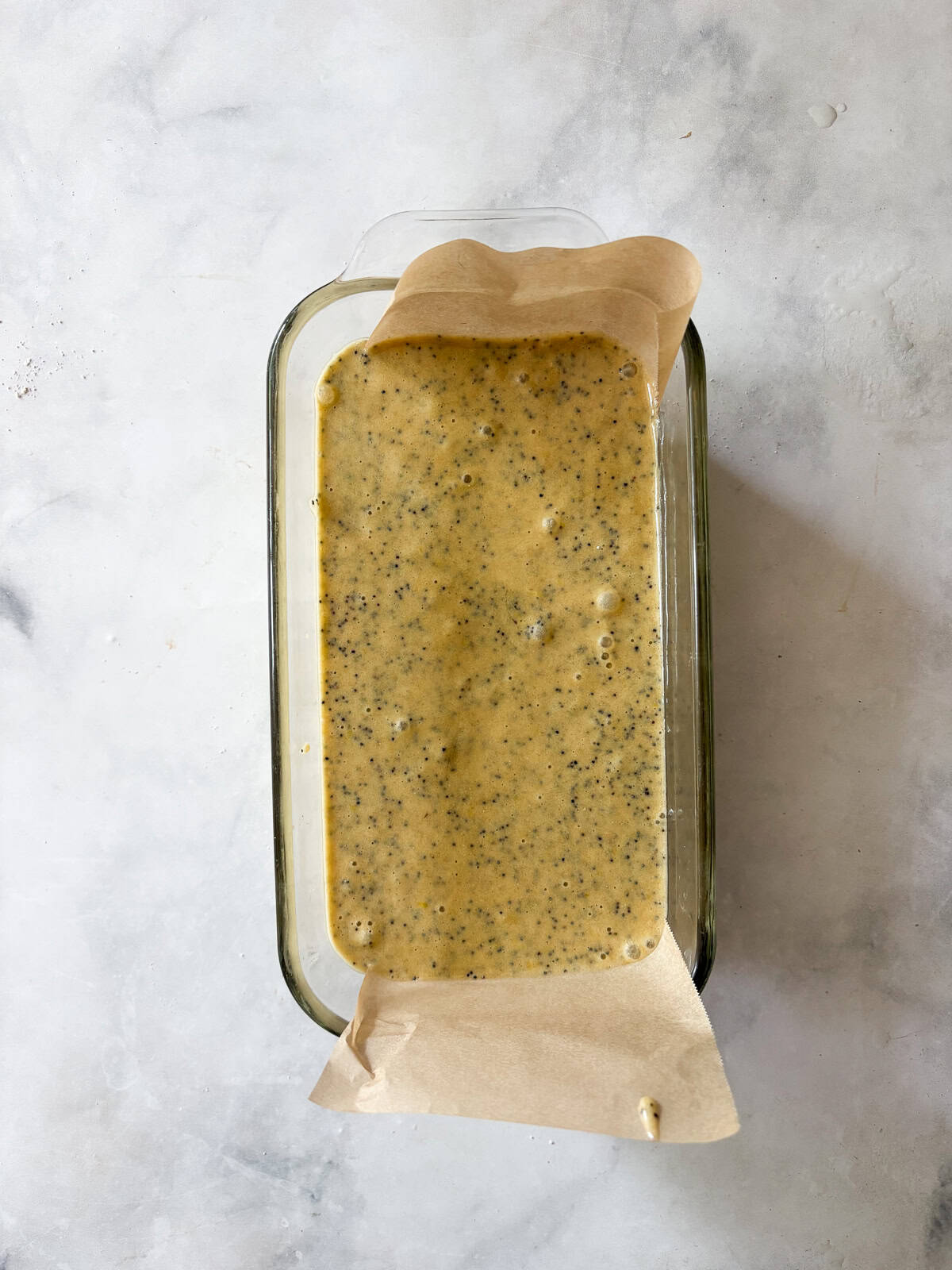 A tender, gorgeously sliceable gluten free lemon poppyseed bread topped with a bright, thick lemon glaze for maximum flavor. Batter for gluten free lemon poppyseed bread in a loaf pan.