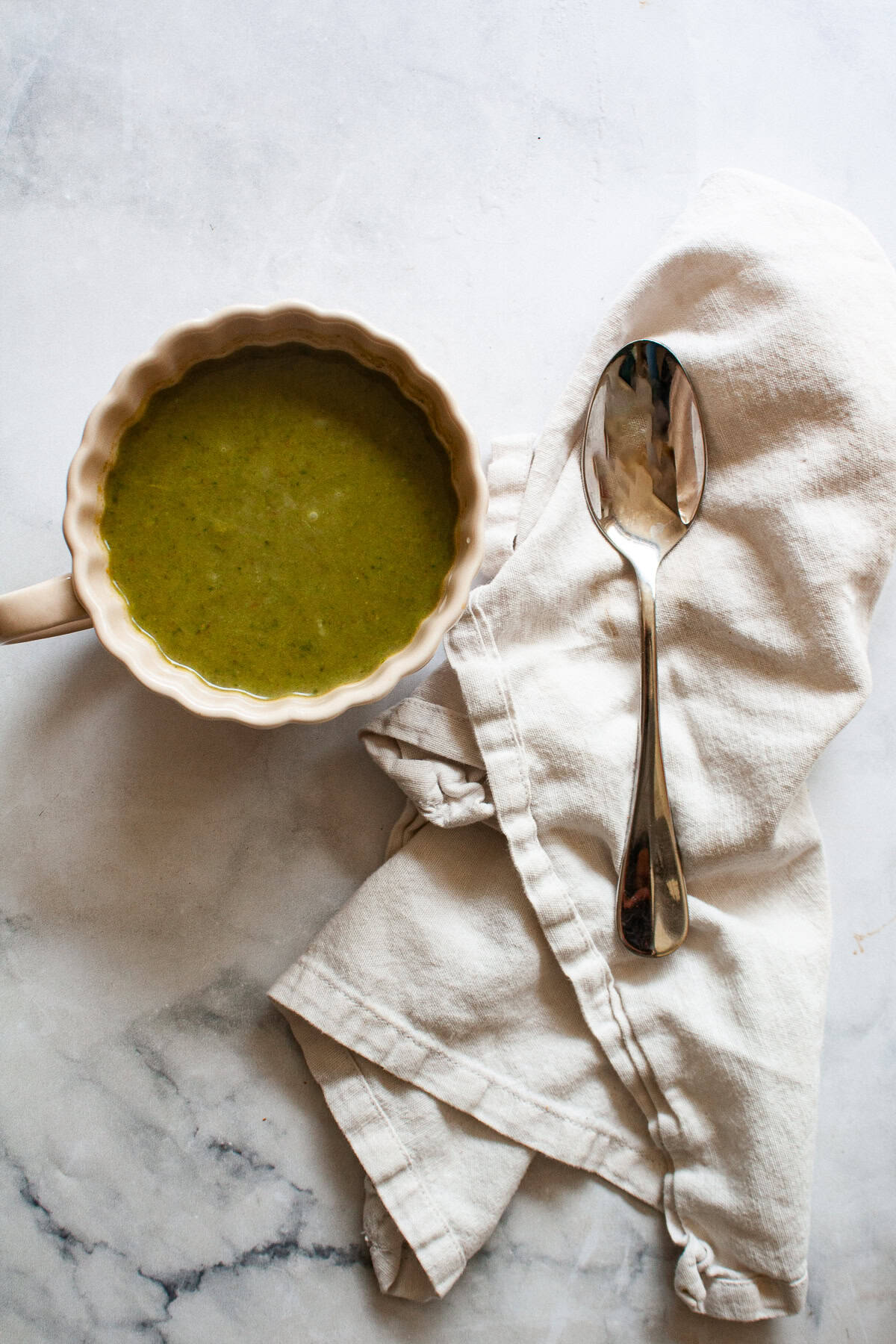 Creamy, vegan asparagus and spinach soup is made with minimal ingredients to create a velvety, nourishing soup that's always welcome. A cup of asparagus and spinach soup and a spoon and napkin.