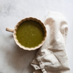 A cup of asparagus and spinach soup next to a white napkin,
