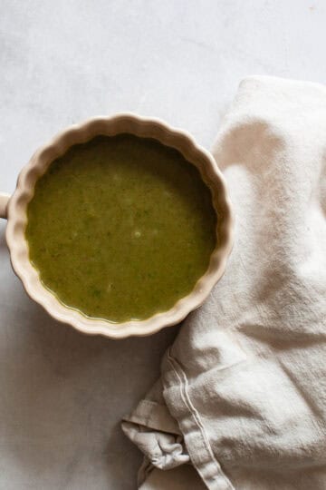 A cup of asparagus and spinach soup next to a white napkin,
