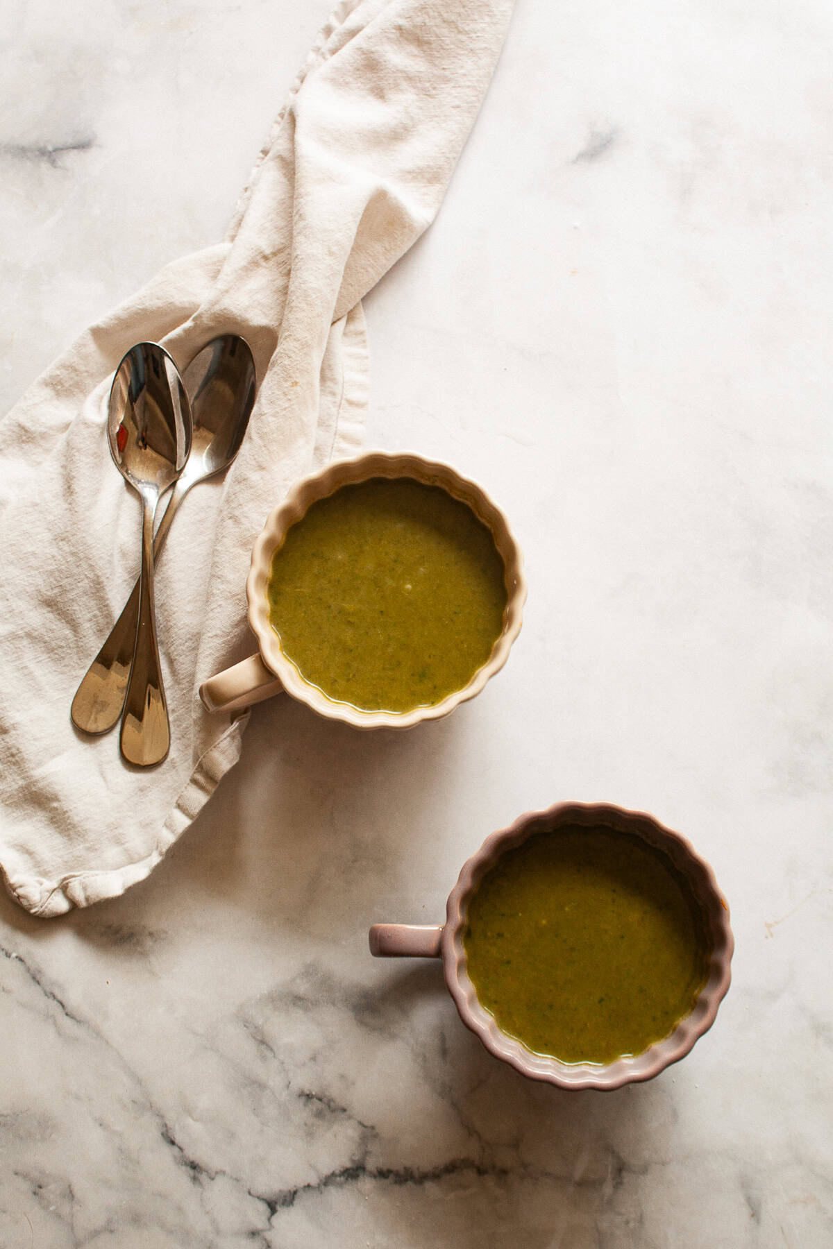Two cups of asparagus and spinach soup next to a napkin with spoons.