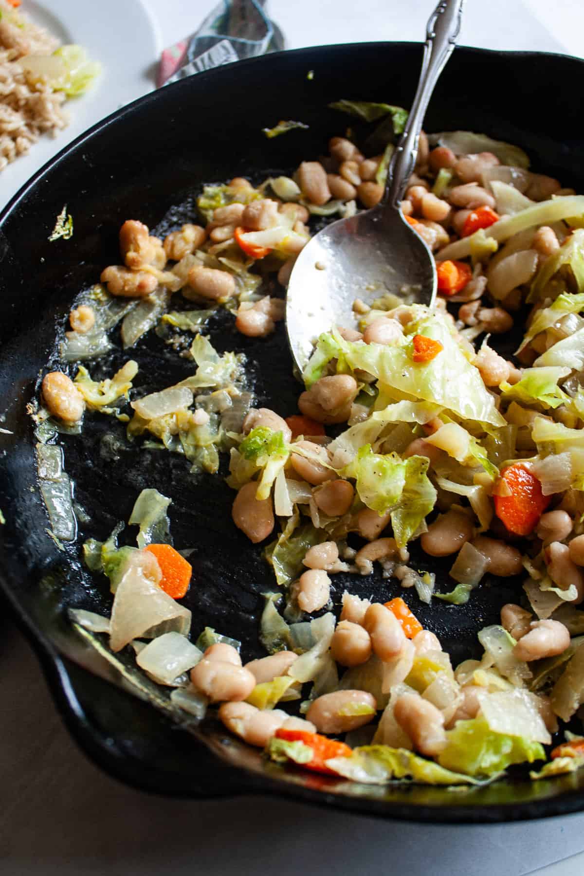 A skillet full of white bean and cabbage stir fry with a spoon in it.