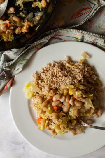 A skillet with white bean and cabbage stir fry next to a plate of stir fry.