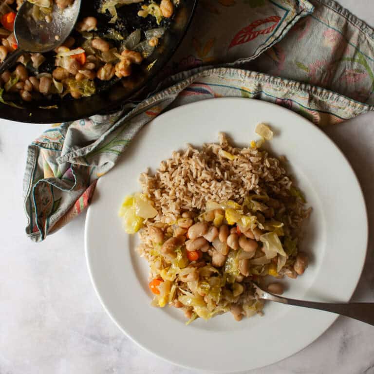A skillet with white bean and cabbage stir fry next to a plate of stir fry.