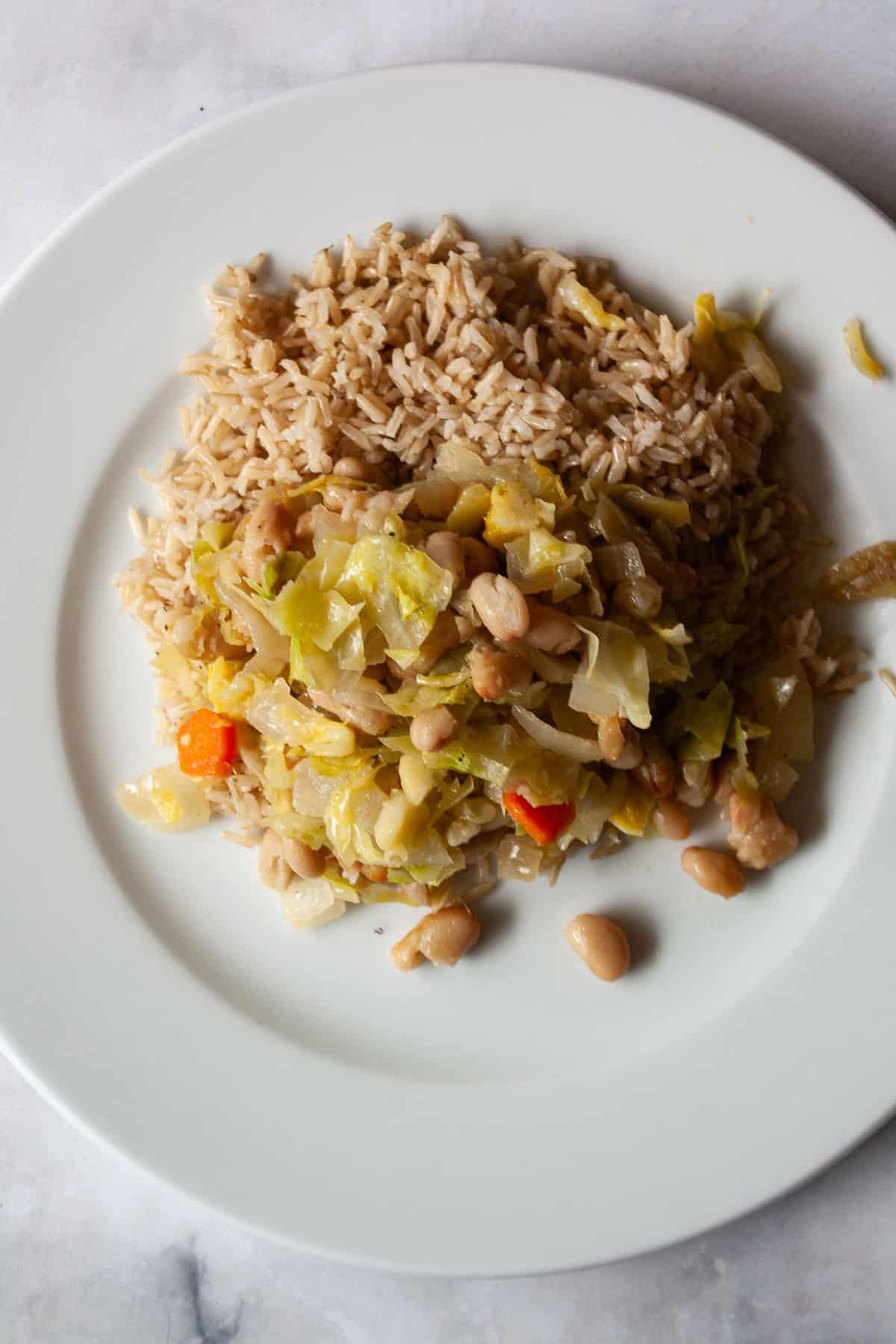 Quick, nourishing, and packed with savory veggies, tender cabbage, and hearty beans, this cabbage stir fry is super satisfying. Vegetarian! A plate holds rice topped with white bean and cabbage stir fry.