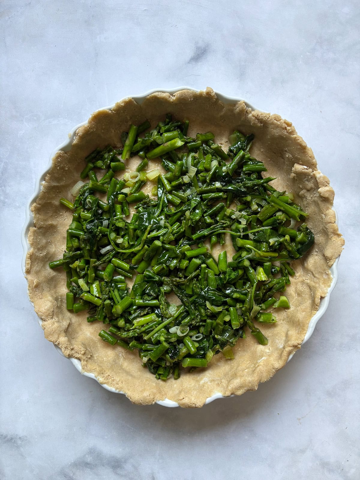 This gluten free asparagus quiche is packed with springy asparagus and salty parmesan cheese to make a wonderful brunch or dinner dish! Assembling a gluten free asparagus quiche in a pan.