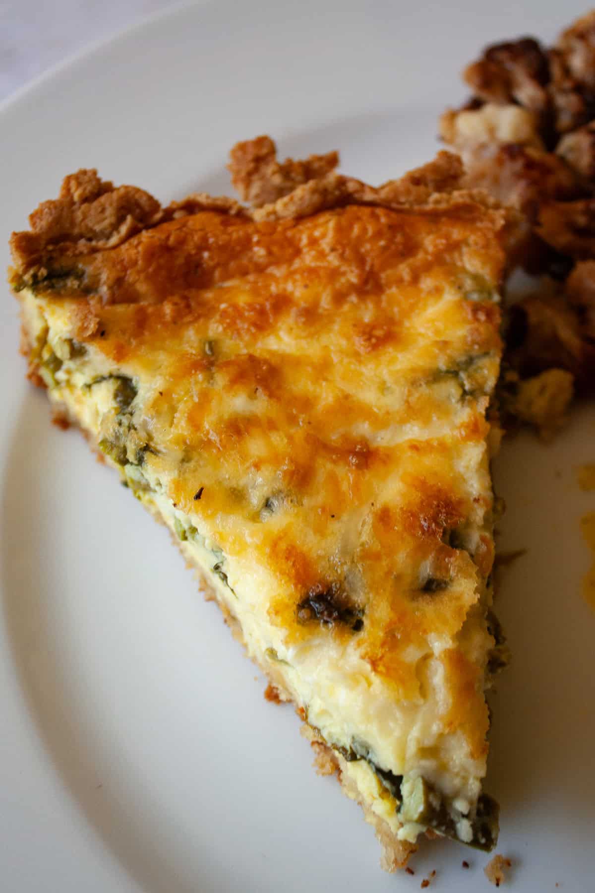 This gluten free asparagus quiche is packed with springy asparagus and salty parmesan cheese to make a wonderful brunch or dinner dish! A slice of gluten free asparagus quiche on a plate.