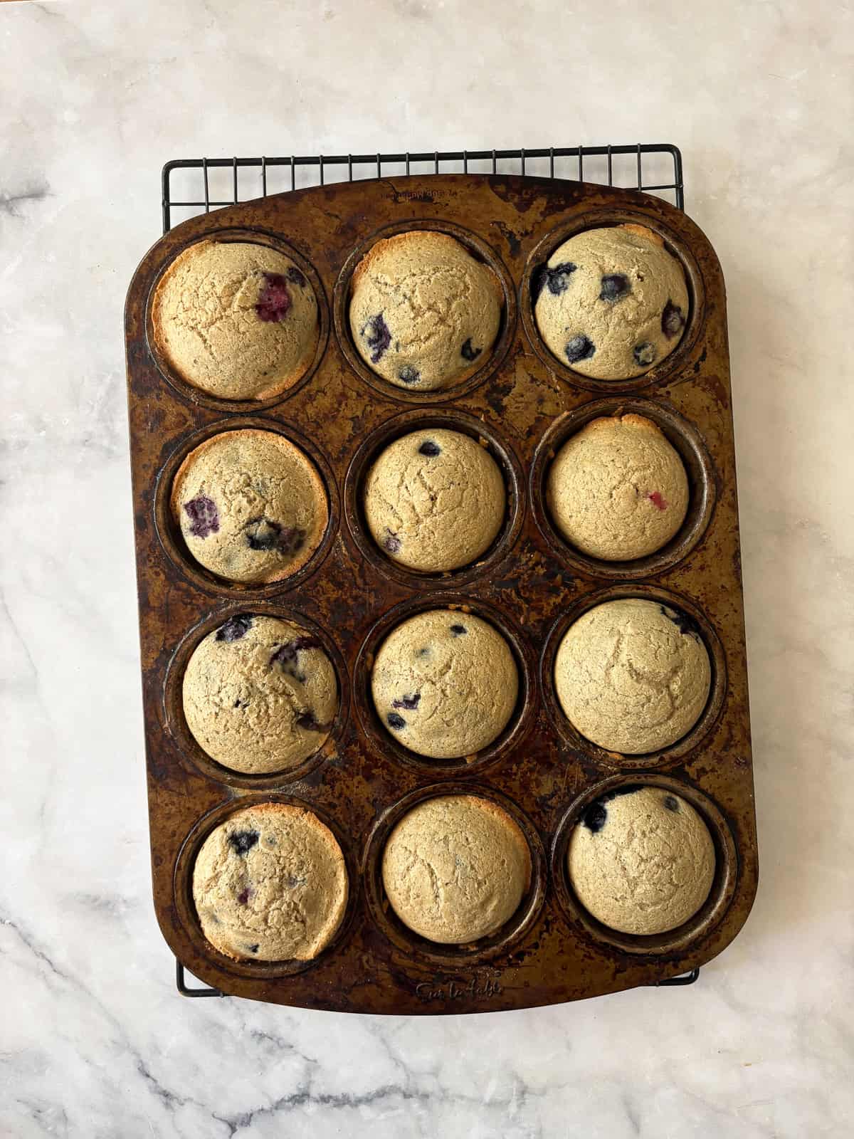 These one-bowl gluten-free berry muffins are made with your choice of whole grain flour and are sweetened just with maple syrup! A muffin tin with baked gluten free berry muffins.