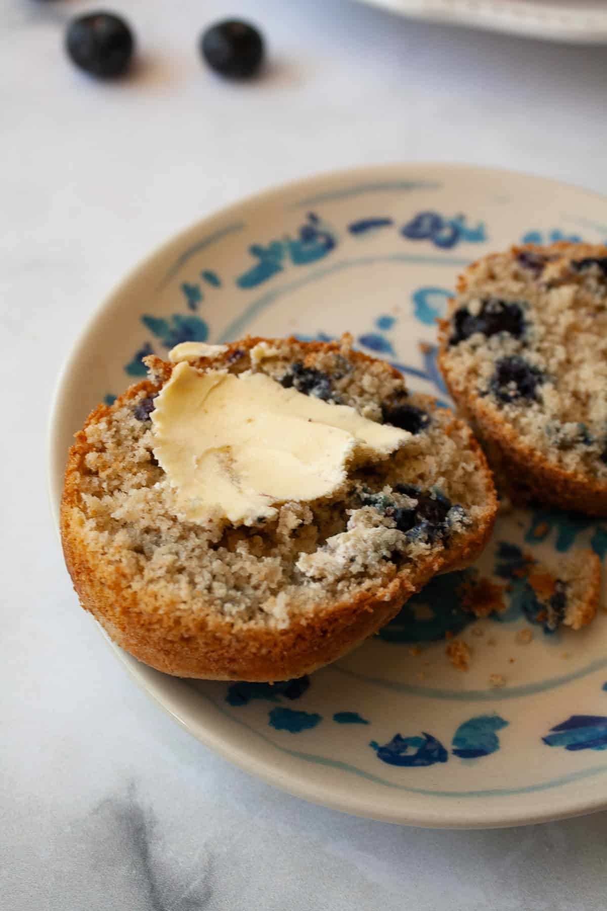 These one-bowl gluten-free berry muffins are made with your choice of whole grain flour and are sweetened just with maple syrup! A bit of butter tops half of a gluten free berry muffin.