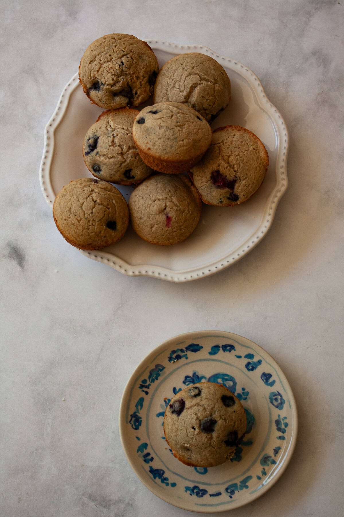 These one-bowl gluten-free berry muffins are made with your choice of whole grain flour and are sweetened just with maple syrup! A plate of gluten free berry muffins and one on a plate.
