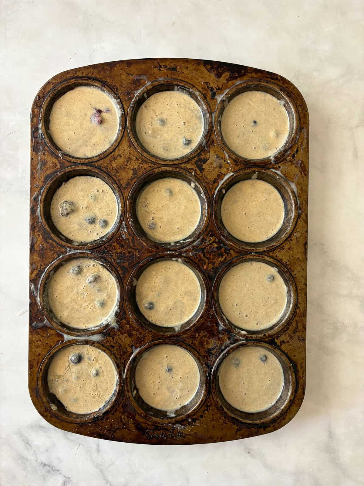 These one-bowl gluten-free berry muffins are made with your choice of whole grain flour and are sweetened just with maple syrup! Gluten free berry muffins batter in a muffin tin.